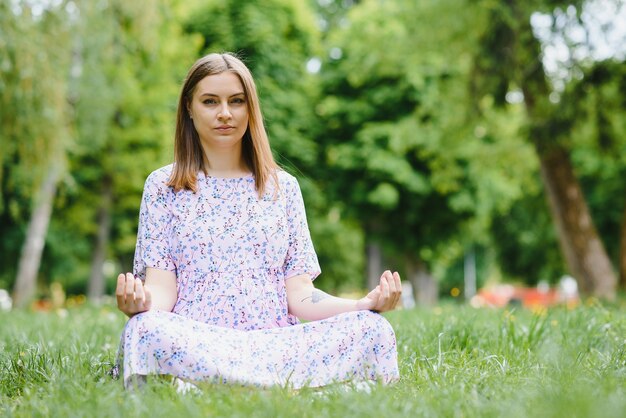 Pregnant woman doing yoga in the park. sitting on the grass.