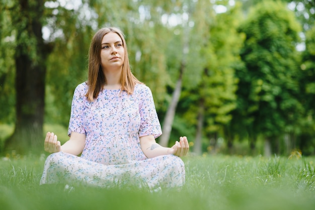 Pregnant woman doing yoga in the park. sitting on the grass.