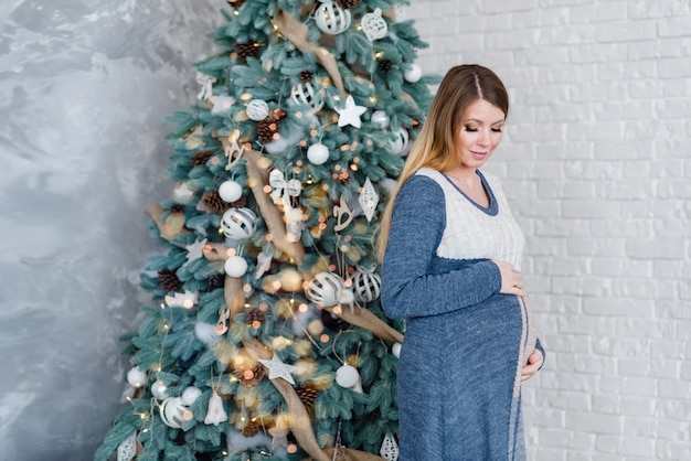 Pregnant woman expecting baby near Christmas tree.