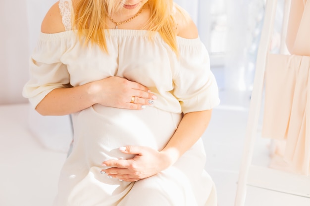 Pregnant woman gently caress her stomach sitting on the chair near a ladder