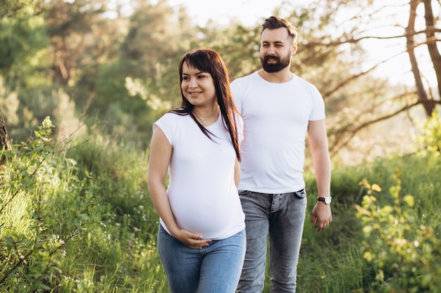 Pregnant woman and her beaeded husband hugging on the tummy together in nature outdoor