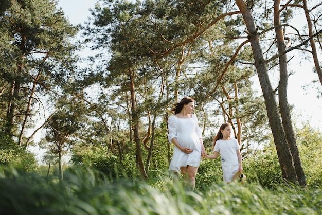 Pregnant woman and her daughter in the park at sunset A happy family