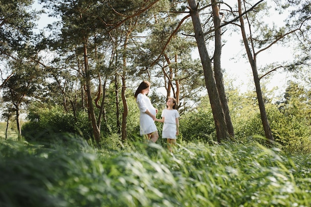 Pregnant woman and her daughter in the park at sunset A happy family