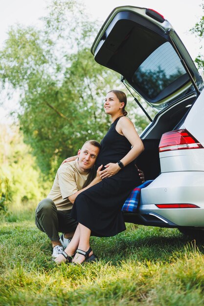 A pregnant woman and her husband are sitting in the trunk of their car in nature A man hugs the belly of his pregnant wife Pregnancy