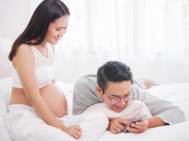 Pregnant woman and her husband useing smartphone at home together