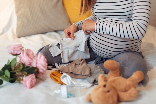 Pregnant woman holding baby bodysuit and packing maternity hospital bag.