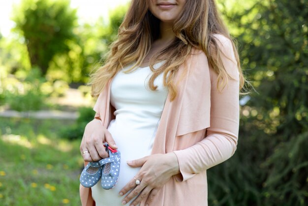 Pregnant woman holding baby boots outdoors at spring nature.