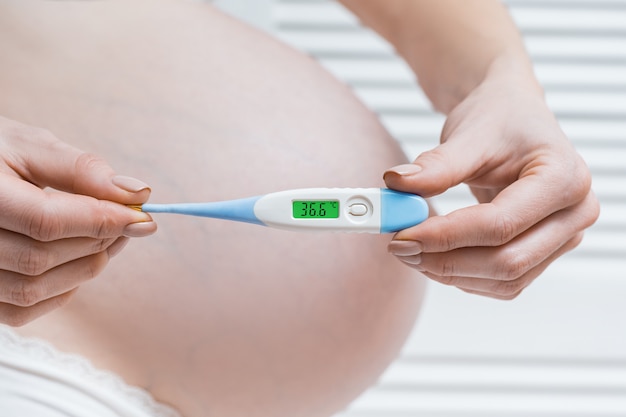 Pregnant woman holding electronic thermometer with normal temperature. Health during pregnancy.