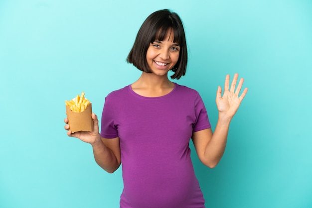 Pregnant woman holding fried chips over isolated background saluting with hand with happy expression