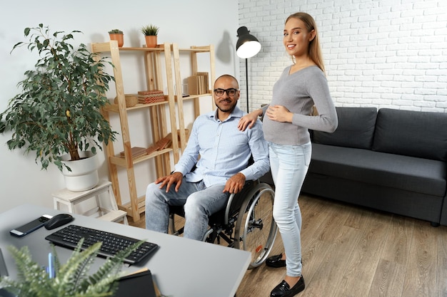 Pregnant woman holding a hand of her disabled husband sitting in a wheelchair