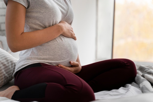 Pregnant woman holding her belly while sitting in bed