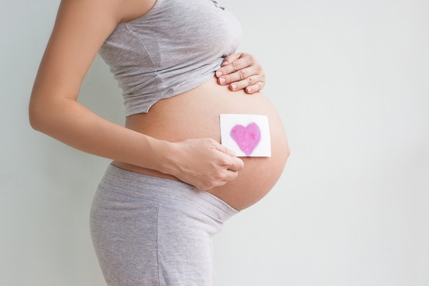 Pregnant woman holding red heart and hand on her belly, symbol of new life