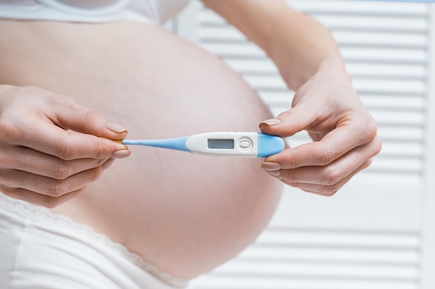 Pregnant woman holding thermometer on background of her belly Health during pregnancy