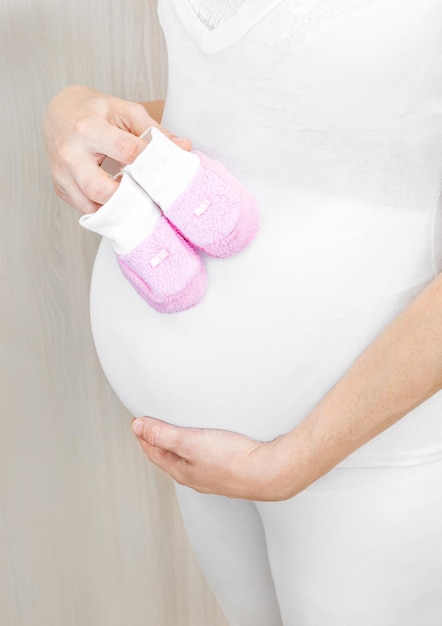 Pregnant woman holds children's shoes on her stomach