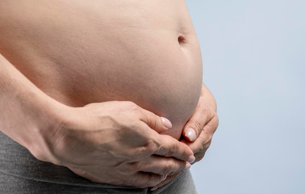 Pregnant woman holds hands on belly on a blue background.