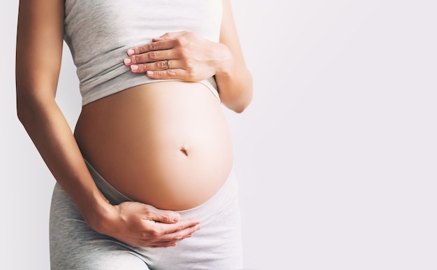 Pregnant woman holds hands on her belly on white background closeup Beautiful photo of pregnancy