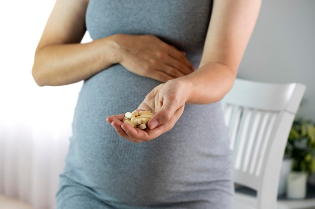 Pregnant woman at home with pills in hands Baby expectation health care and prenatal vitamins on pregnancy time Illness and medicine while pregnancy