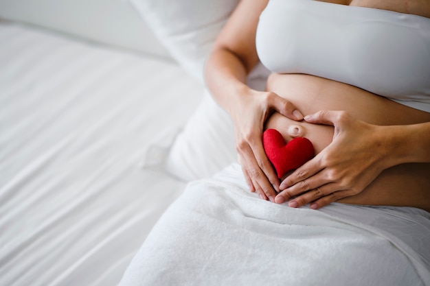 Pregnant woman is happy to take care of the child at birth.Happy pregnant woman is touching her belly.Pregnant woman show love by making a heart shape on their belly.