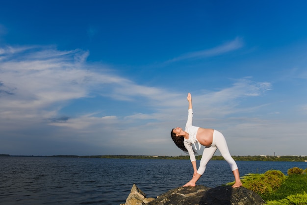 Pregnant woman is practicing yoga beside river