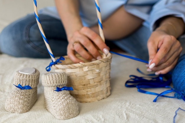 A pregnant woman is preparing a gift for her unborn child. Puts baby booties in a wicker basket.