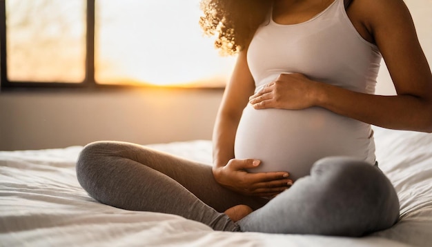 a pregnant woman is sitting on a bed with the sun shining behind her