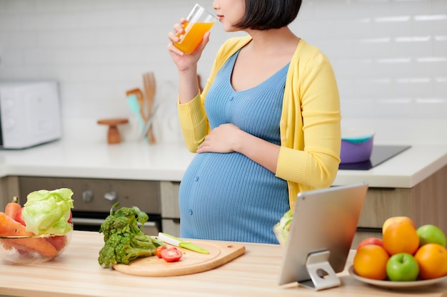 Pregnant woman on kitchen drinking healthy fruit juice