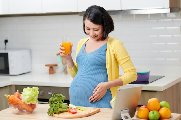 Pregnant woman on kitchen drinking healthy fruit juice