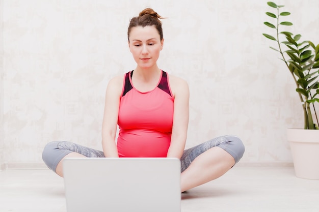 Pregnant woman makes yoga practice online class at home Looks at the laptop in yoga pose