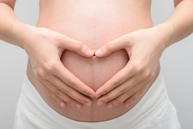 Pregnant woman making hand gesture a heart shape on her belly