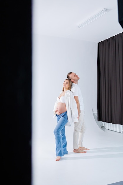 A pregnant woman and a man are standing on a white background Beautiful young attractive pregnant woman Family marriage childbirth concept Happy pregnant couple