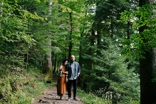 Pregnant woman and man walk on the path on the slope in the park