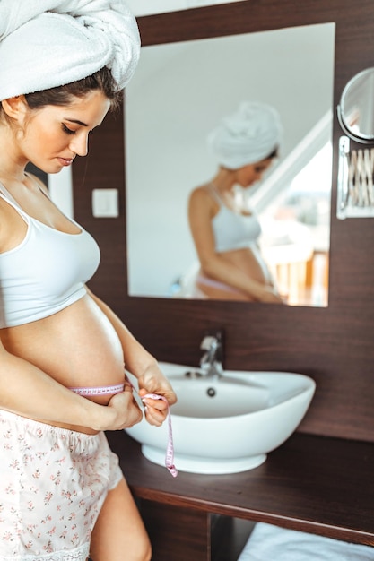 Pregnant woman measuring her belly in the bathroom