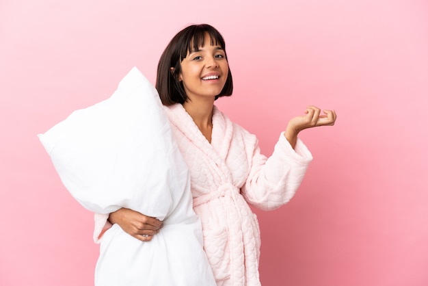 Pregnant woman in pajamas isolated on pink background extending hands to the side for inviting to come