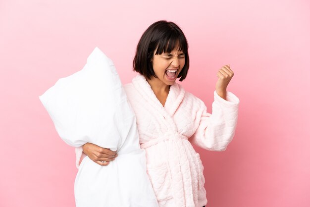 Pregnant woman in pajamas isolated on pink wall celebrating a victory