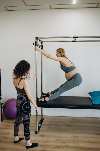 Pregnant woman pilates reformer roll up cadillac exercise with personal trainer