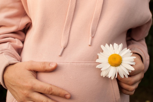 A pregnant woman in a pink blouse holds her stomach and a daisy closeup with her hand