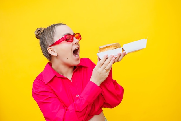 A pregnant woman in a pink shirt and jeans is holding a tasty burger Harmful food during pregnancy Concept of easy and happy pregnancy