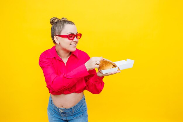 A pregnant woman in a pink shirt and jeans is holding a tasty burger Harmful food during pregnancy Concept of easy and happy pregnancy