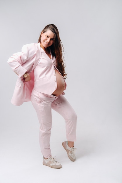 Pregnant woman in pink suit close-up on gray background.