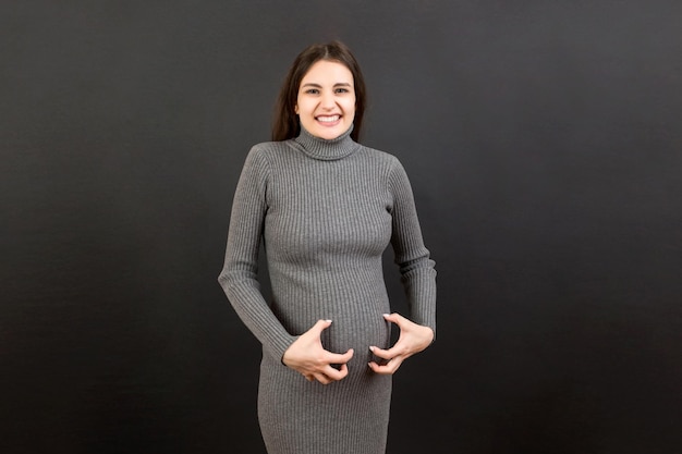 Pregnant woman scratching her belly on colored background