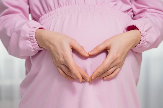 Pregnant woman shows fingers heart near big bump with baby