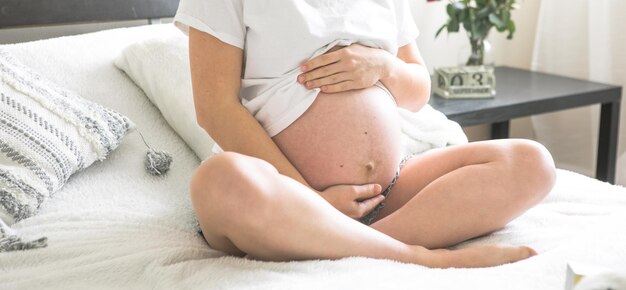 Pregnant woman sitting on a bed holding The concept of pregnancy motherhood and prenatal care Mom with a new life