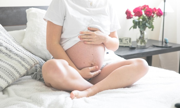 Pregnant woman sitting on a bed holding The concept of pregnancy motherhood and prenatal care Mom with a new life