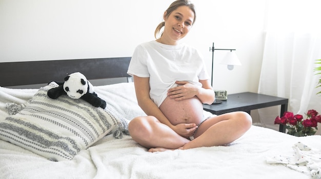 Pregnant woman sitting on a bed holding The concept of pregnancy motherhood and prenatal care Mom with a new life