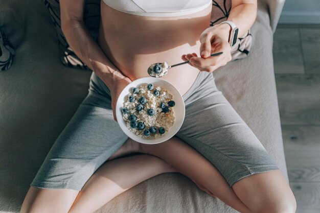 Pregnant woman sitting on the sofa and holding a plate with ricotta and blueberries