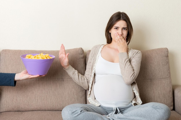 Pregnant woman sitting on the sofa refuses to eat unhealthy snacks Stop to the junk food during pregnancy concept