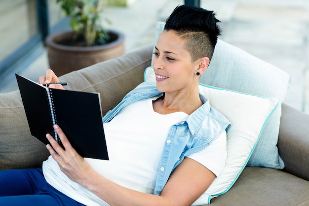 Pregnant woman sitting on sofa and writing on notepad