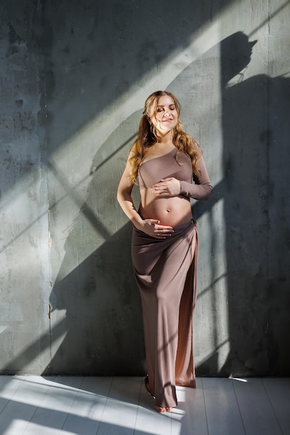 A pregnant woman in a skirt hugs her stomach with her hands Fashion pregnant woman Full length portrait on gray background Happy pregnancy