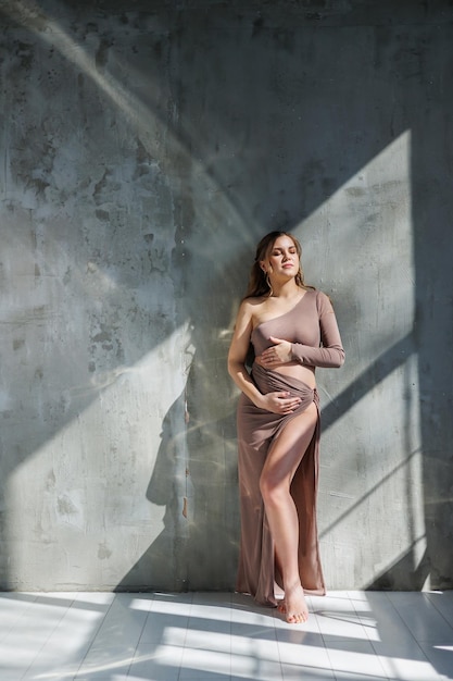 A pregnant woman in a skirt hugs her stomach with her hands Fashion pregnant woman Full length portrait on gray background Happy pregnancy