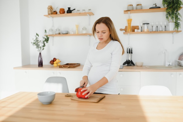 Pregnant woman slicing vegetables at home in the kitchen